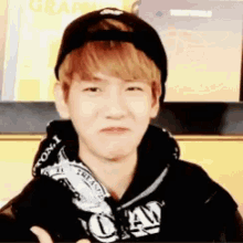 a young man wearing a baseball cap and a hoodie is making a face .