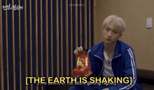a man in a blue jacket is holding a toy and the words the earth is shaking are above him