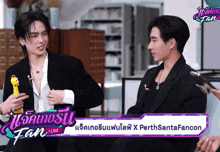 two men are sitting next to each other in front of a sign that says fan