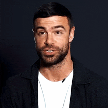 a man with a beard is wearing a black jacket and a white t-shirt