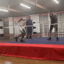 two men are wrestling in a boxing ring with a referee watching