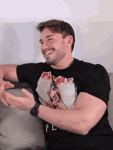 a man is sitting on a couch wearing a black playboy t-shirt and laughing .