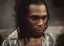 a man with dreadlocks is wearing a snakeskin shirt and necklace .
