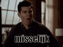 a man is making a funny face while standing in front of a window and a sign that says misseljik .