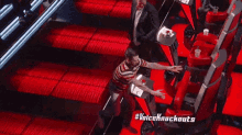 a man in a suit stands in front of a row of red chairs with the words #voiceknockouts written on the bottom