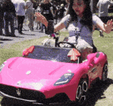 a woman is sitting in a pink toy car with the letter m on the front