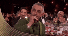 a man in a green jacket is sitting at a table with wine glasses and a sign that says n live