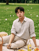 a man sits on a blanket in the grass with a bottle of lemonade