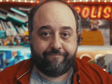 a bald man with a beard wearing headphones stands in front of a neon sign that says polic