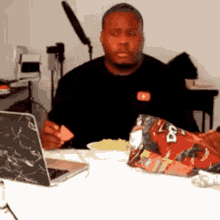 a man is sitting at a table with a bag of doritos and a laptop
