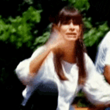 a woman in a white shirt is sitting on a bench and waving .