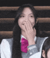 a girl with long black hair is covering her mouth with her hand .