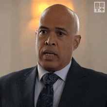 a man in a suit and tie is looking at the camera with a be it logo behind him