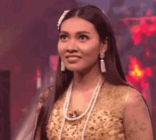 a woman with long hair is wearing a gold dress and pearls and earrings .