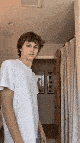 a young man in a white t-shirt stands in a doorway