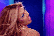 a close up of a woman 's face with her hair blowing in the wind in front of a purple wall .