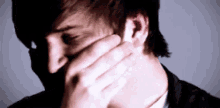 a close up of a man covering his face with his hand .