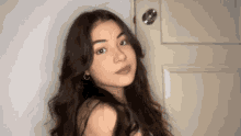 a young woman with long dark hair is standing in front of a door