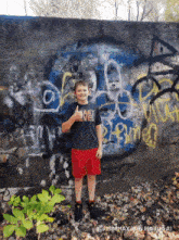 a young boy stands in front of a wall with graffiti on it and a shirt that says last level