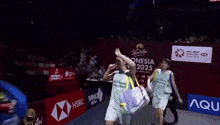 a man wearing a petronas shirt walks across a badminton court
