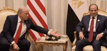 two men in suits and ties are sitting in front of a flag