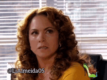 a woman with curly hair is sitting in front of a window and has the username lialmeida05