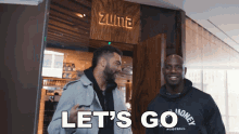 two men standing in front of a zuma restaurant with the words let 's go