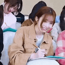 a group of women are sitting in a classroom laughing and writing on a clipboard .