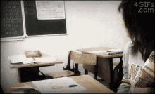 a girl in a w sweatshirt sits at a desk in front of a chalkboard