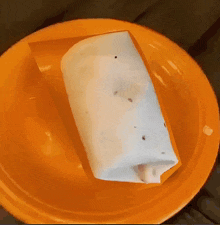 an orange plate with a burrito wrapped in wax paper