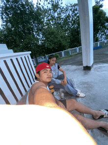 a man wearing a red new era hat sits next to another man