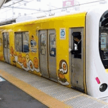 a yellow train with cartoon characters on the side is sitting on a train platform .