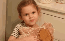 a little girl is holding a teddy bear and making a face .