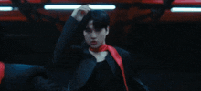 a young man wearing a black shirt and a red scarf is dancing in a dark room .