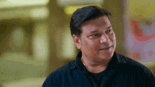 a man in a black shirt is smiling and looking at the camera .