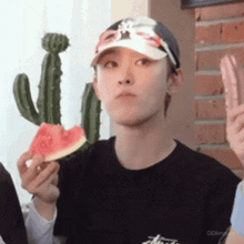 a young man is eating a slice of watermelon while wearing a hat .