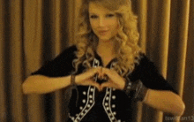 a woman making a heart with her hands in front of a curtain