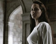 a woman with long hair and a white shirt is standing in front of a window .