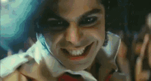 a close up of a man with black eyes and a white shirt smiling at the camera .
