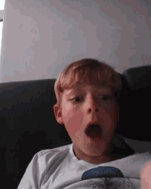 a young boy is laying on a couch with his mouth open