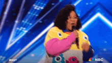 a woman singing into a microphone on a stage with a nbc logo in the corner