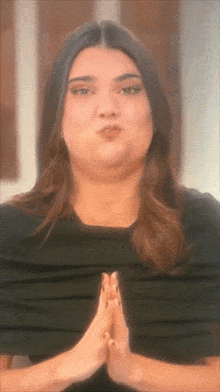 a woman in a black shirt is making a face with her hands folded