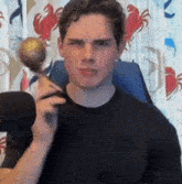 a man in a black shirt is holding a spoon over his shoulder and looking at the camera .