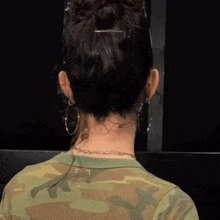 a woman wearing a camouflage shirt and earrings is standing in front of a black wall .