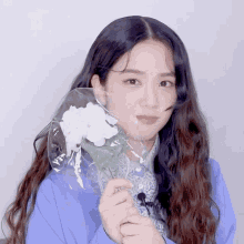 a woman in a blue jacket is holding a white flower