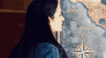 a woman in a denim jacket is looking at a map of the world .