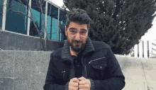 a man with a beard is wearing a black jacket and a grey sweater