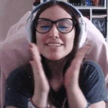 a woman wearing headphones and glasses is smiling and clapping .