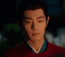 a close up of a man wearing a red jacket and a blue shirt