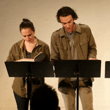 a man and a woman are standing at a podium reading a script